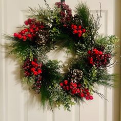 a wreath hanging on the front door decorated with berries and pineconis for christmas