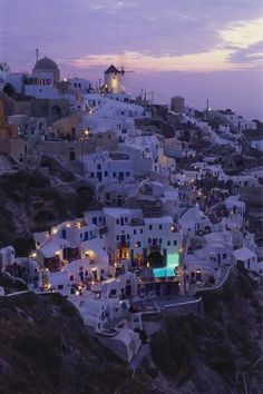 an aerial view of white buildings on the hillside at dusk, with lights in the windows