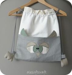 a gray and white cat drawstring bag hanging on a wooden hanger with the word interest written below it