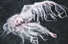 a woman with long white hair laying on the ground