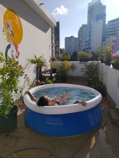 a woman laying in an above ground swimming pool on a roof top deck with city buildings behind her