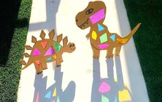 two cardboard dinosaurs are standing on the ground with their shadows projected on them and one has its head turned to look like a dinosaur