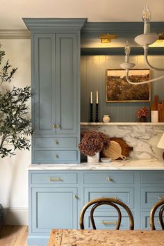 a kitchen with blue cabinets and white marble counter tops, an olive tree is in the corner