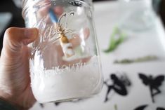 a person holding up a mason jar filled with white liquid on top of a table