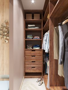 a walk in closet with wooden drawers and clothes hanging on the wall next to it