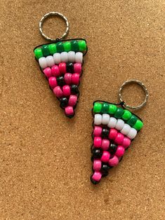 two pieces of colorful beads are sitting on a corkboard surface, one is shaped like a slice of pizza