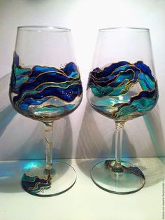 two wine glasses sitting next to each other on top of a white table with blue and gold designs