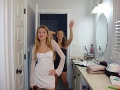 two young women are standing in the bathroom and one is wearing a short white dress