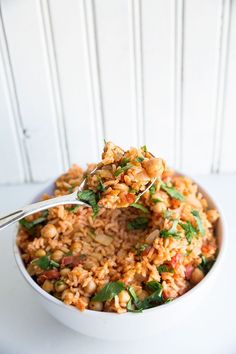 a white bowl filled with rice and garnished with green leafy greens, on top of a white table