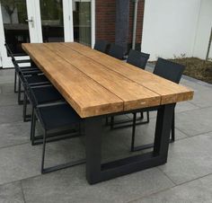 a wooden table sitting on top of a patio next to a brick building with black chairs