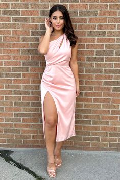 a woman standing in front of a brick wall wearing a pink dress with thigh high slit