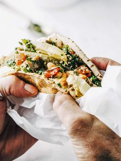 a person is holding a pita sandwich with vegetables and other toppings on it