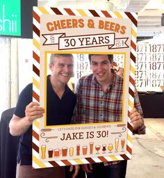 two men standing next to each other holding up a sign with cheers and beers written on it