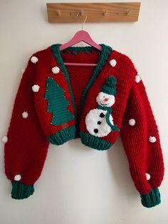 a red sweater with snowman and christmas tree on it hanging from a wooden hanger