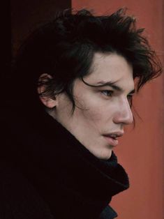 a young man with black hair is looking at the camera while wearing a coat and scarf