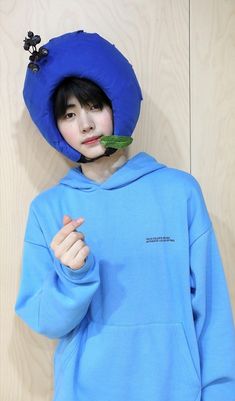 a woman wearing a blue hoodie with a flower in her mouth, standing next to a wooden wall