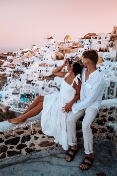 a man and woman sitting on a stone wall next to each other near the ocean