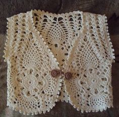 a white crocheted vest with buttons on the front and back, sitting on top of a brown blanket