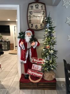 a santa clause standing next to a christmas tree in front of a clock on the wall