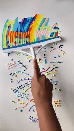 a hand is holding a brush with colorful designs on it and pointing to the side