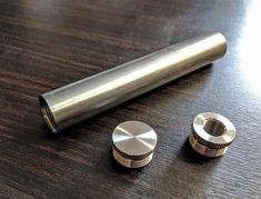 two metal knobs sitting on top of a wooden table next to a silver tube