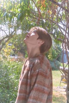 a young man standing in front of a tree looking up at the sky with his eyes closed