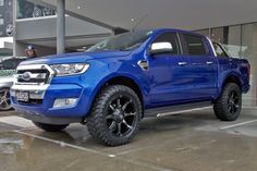 a blue truck parked in front of a building with other cars behind it on display