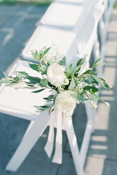 white flowers and greenery are tied to the back of a bench for an outdoor ceremony