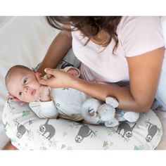 a woman holding a baby in her arms on top of a white bed with an elephant pillow