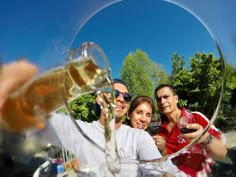 three people are taking a selfie in front of a wine glass with the reflection of trees behind them