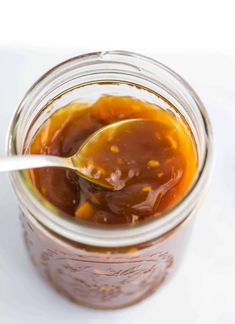 a spoon is in a jar filled with peanut butter and jelly sauce on a white surface