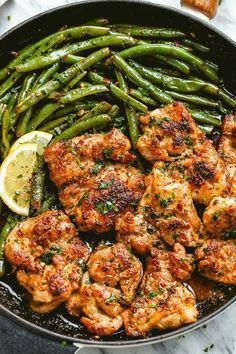 chicken and green beans in a skillet with lemon wedges