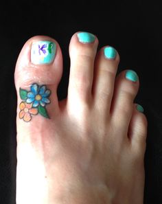 a woman's foot with blue and green flowers on it, next to her toe