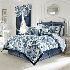 a bed with blue and white comforter in a bedroom next to a mirror on the wall