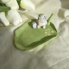 a small ceramic animal sitting on top of a green plate next to white tulips