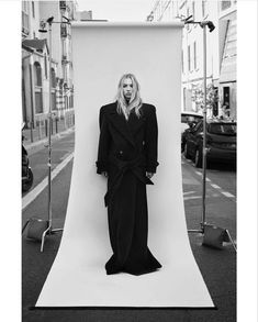 a black and white photo of a woman standing in front of an empty backdrop on the street