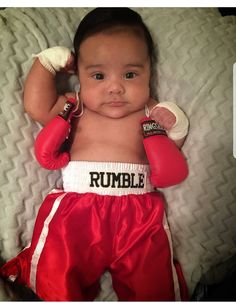 a baby wearing boxing gloves laying on top of a white blanket with the words rumble written on it