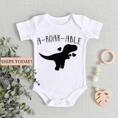 a baby bodysuit with the words a roar - able ship today on it next to some plants