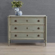 an old dresser with flowers on top in front of a gray wall and wooden floor