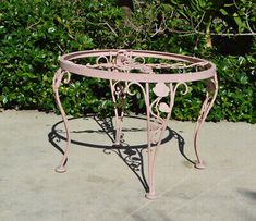 a pink metal table sitting on top of a cement ground next to bushes and trees