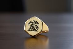 Embark on a legendary quest with our Custom Gold Hexagon Shaped Signet Ring, masterfully engraved with a knight battling a dragon. This ring captures the essence of epic medieval tales and fantasy lore, making it a perfect collectible for fans of chivalry, dragons, and royal adventures. Crafted from high-quality gold, the hexagon shape provides a modern twist on a classic theme, offering a bold statement piece that commands attention. Whether you're a lover of fantasy novels, a medieval reenacto Medieval Engraved Signet Ring Gift, Medieval Engraved Signet Ring For Gift, Warrior Ring, Dna Jewelry, Fantasy Ring, Dragon Ring, Fancy Gifts, Fantasy Novels, Unisex Ring