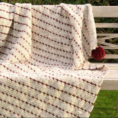 a crocheted blanket sitting on top of a wooden bench next to a red pom - pom