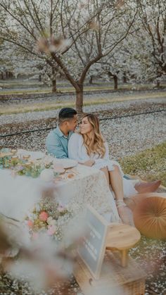 a man and woman sitting at a table in the middle of an apple orchard with flowers on it