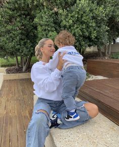 a woman sitting on top of a wooden bench holding a child