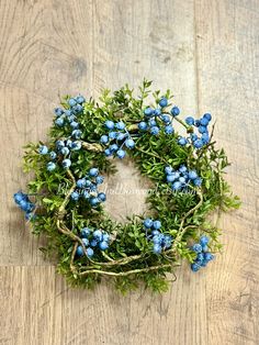 a wreath with blue flowers and green leaves on a wooden surface, ready to be used as an ornament