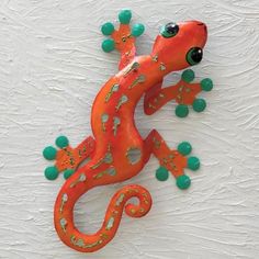 an orange and green gecko sitting on top of a white wall