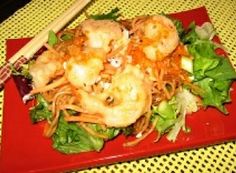 a red plate topped with shrimp and veggies next to chopsticks on a table