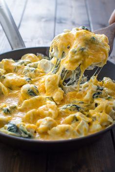 a spoon full of cheese and spinach being lifted from a skillet with a spatula