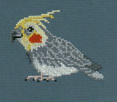 a cross stitch bird with yellow and gray feathers on it's head is shown