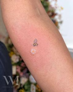 a small tattoo on the arm of a person with a bee and daisies in it